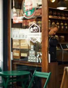 View of a cozy coffee shop window displaying products and a barista working inside.