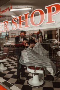 A barber is giving a haircut inside a classic barbershop, captured through the window.