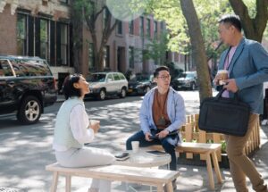 Three colleagues enjoying a coffee break on a shaded city street, engaging in conversation.